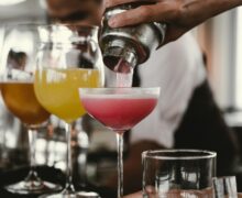 person holding cocktail shaker pouring liquid in glass during daytime